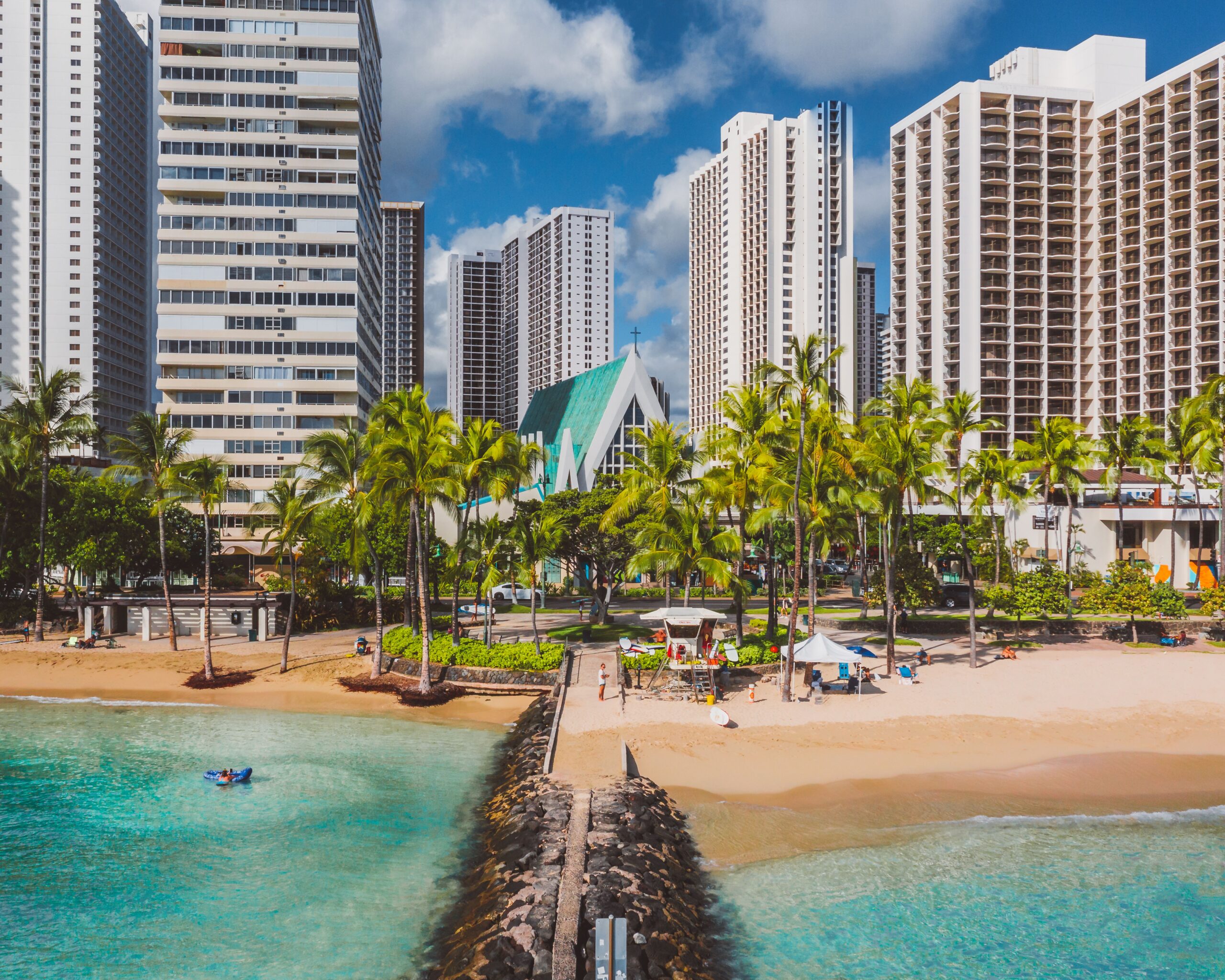 Photo-of-a-tropical-beach-shore-with-palm-trees-and-modern-city-skyscrapers-in-the-background